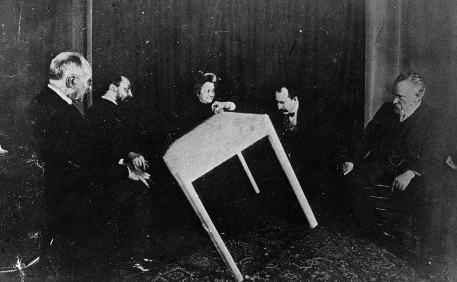 A table moves of its own accord during a séance.