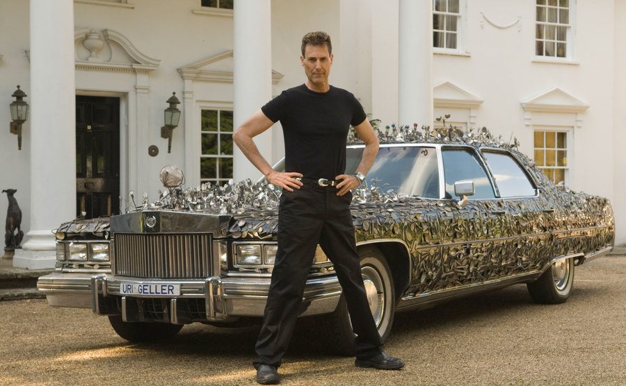Uri Geller poses with his custom-built Cadillac encrusted with bend spoons.