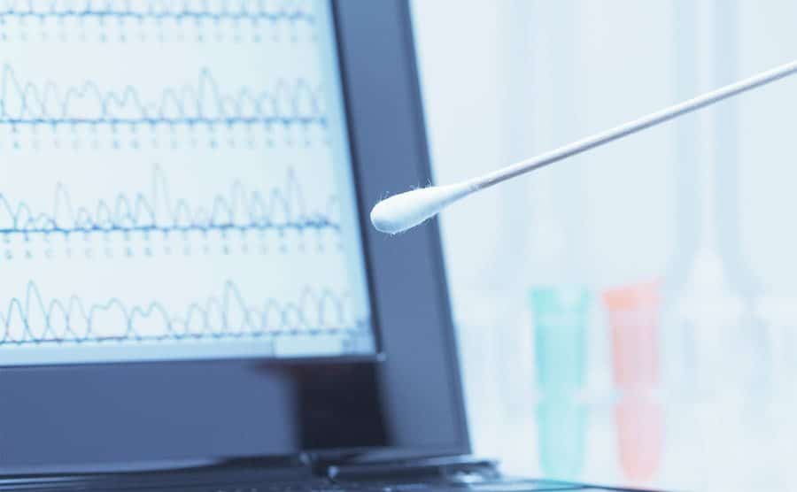 A cotton swab with saliva is placed in front of a laptop screen