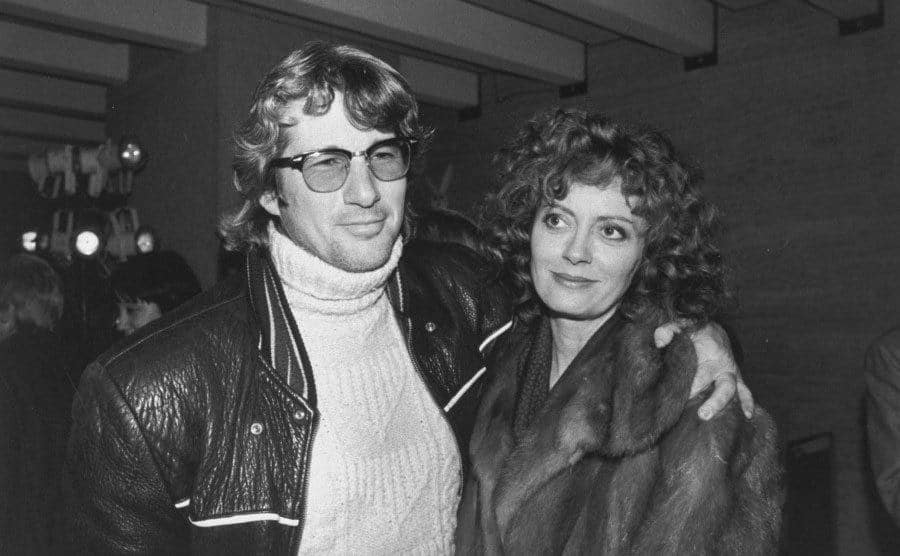 Chris Sarandon and Susan Sarandon embrace each other at a bar.