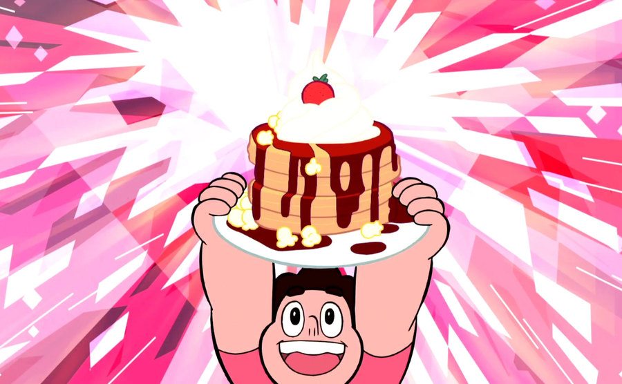Steven Universe holds a plate of pancakes over his head.