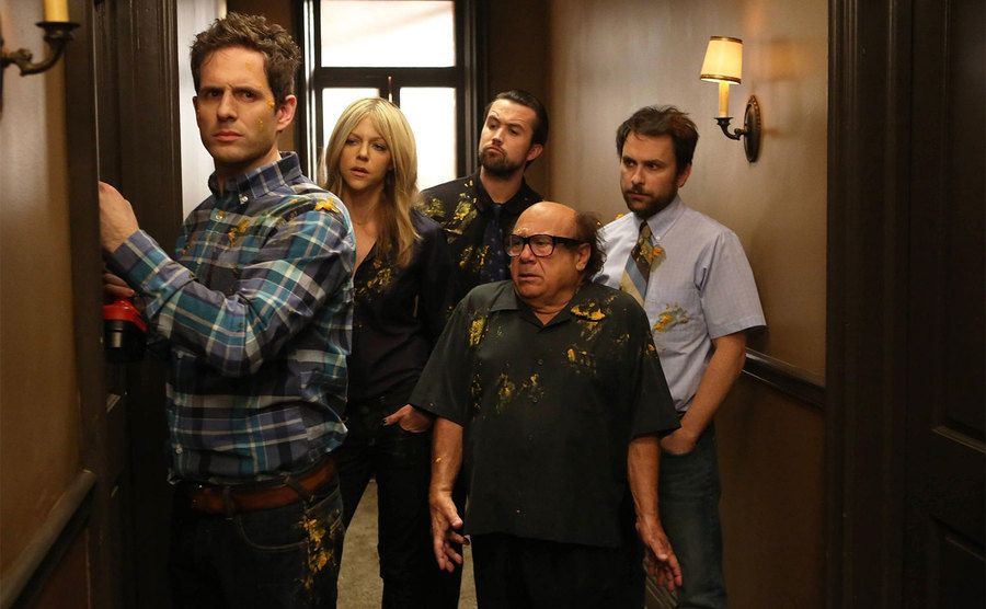 Dennis, Deandra, Mac, Frank, and Charlie stand in an apartment building hallway.