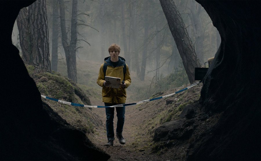 Louis Hofmann, as Jonas Kahnwald, stands at the opening of a cave.