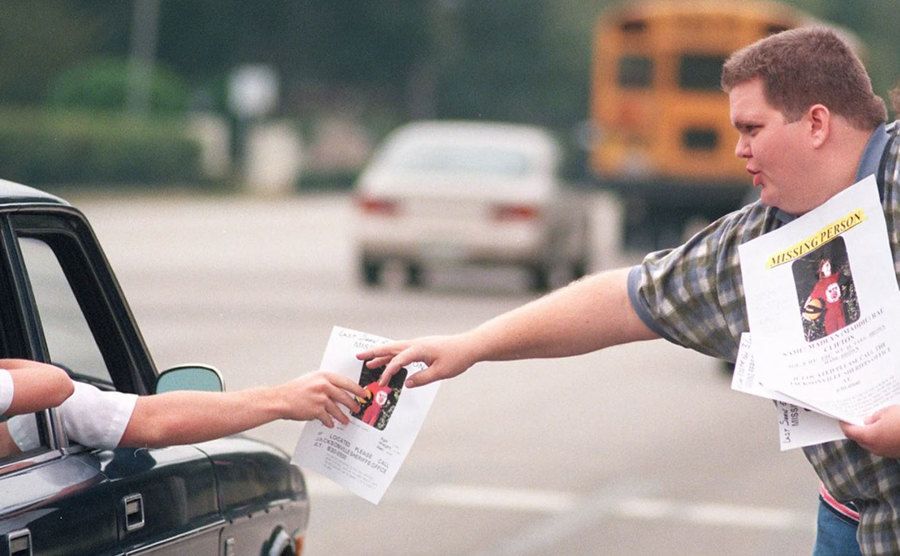 An image of a neighbor handing out missing person posters to cars. 