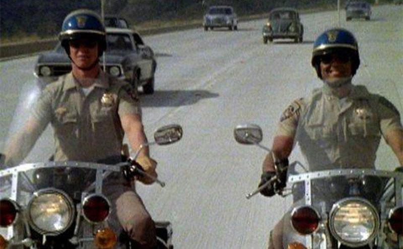 A still of Larry Wilcox and Erik Estrada riding their bikes.
