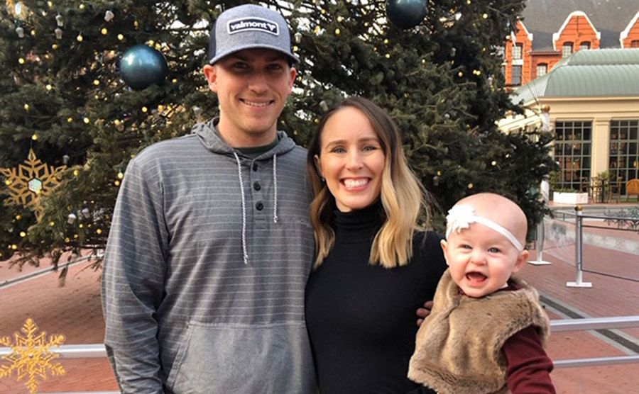 Danielle Bergman, Bobby Dodd, and their daughter pose in front of a Christmas tree.
