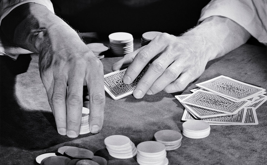Man hands are playing a game of cards while sitting at a poker table.