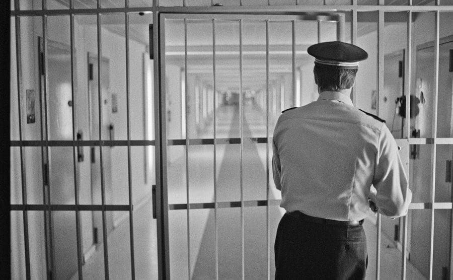 A guard opens a locked gate leading to prisoner's cells.