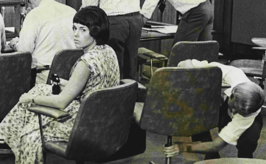 Lindy looks around, and Michael adjusts his chair in the courtroom.