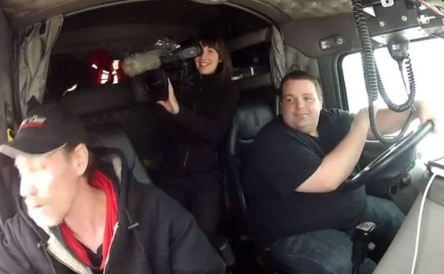 A still of Leia Hutchings holding a camera while riding on a truck.