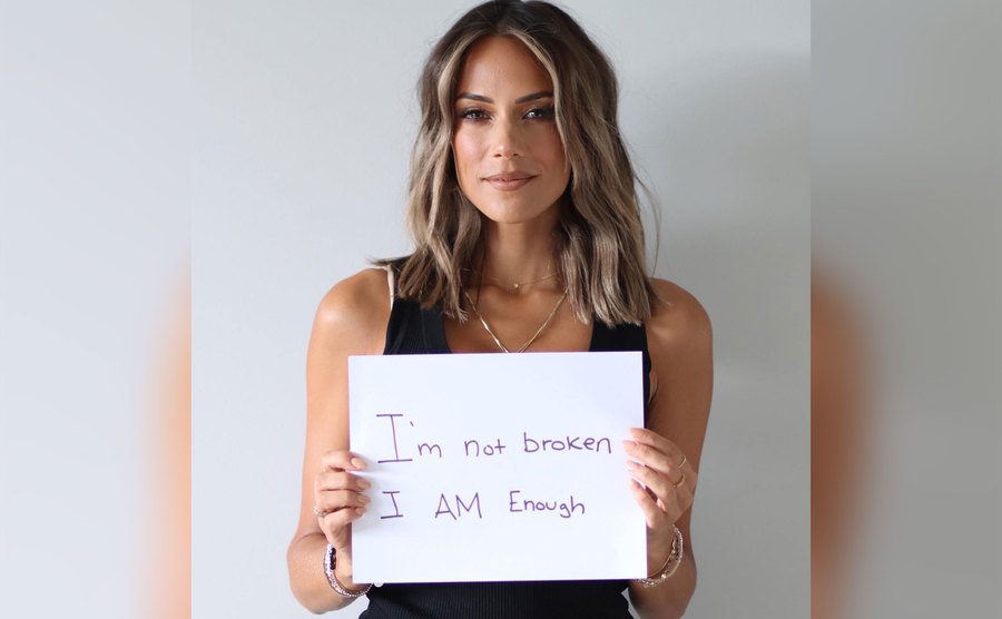 Jana Kramer holds up a sign that says “I’m not broken I am enough”.