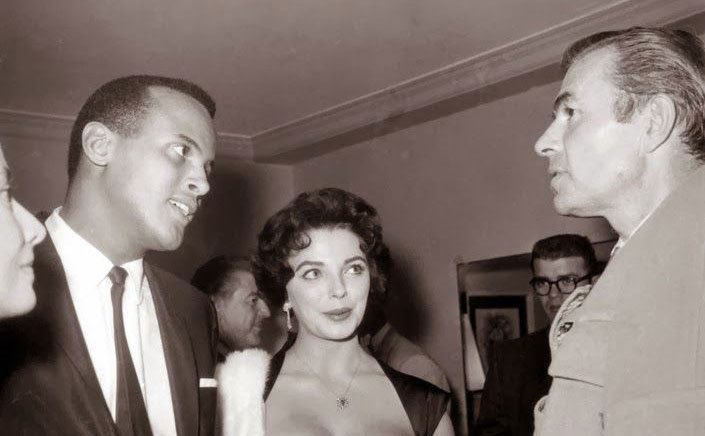 Harry Belafonte and Joan Collins talk to guests at a party.
