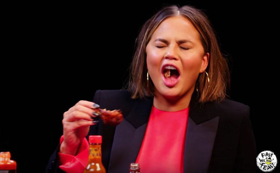 Chrissy Teigen struggles to swallow her wing. 