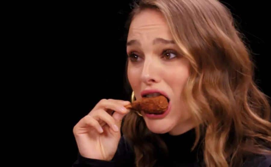 Natalie Portman holds back tears as she takes a wing bite. 