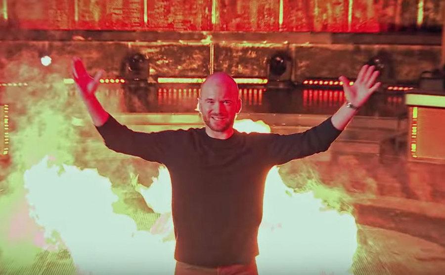 Evans enters the stage in front of burning flames. 