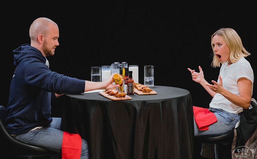 Kristen Bell looks shocked that Evans is adding more sauce to his wings. 