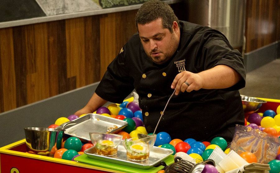 A competitor cooks while standing inside a ball pit.