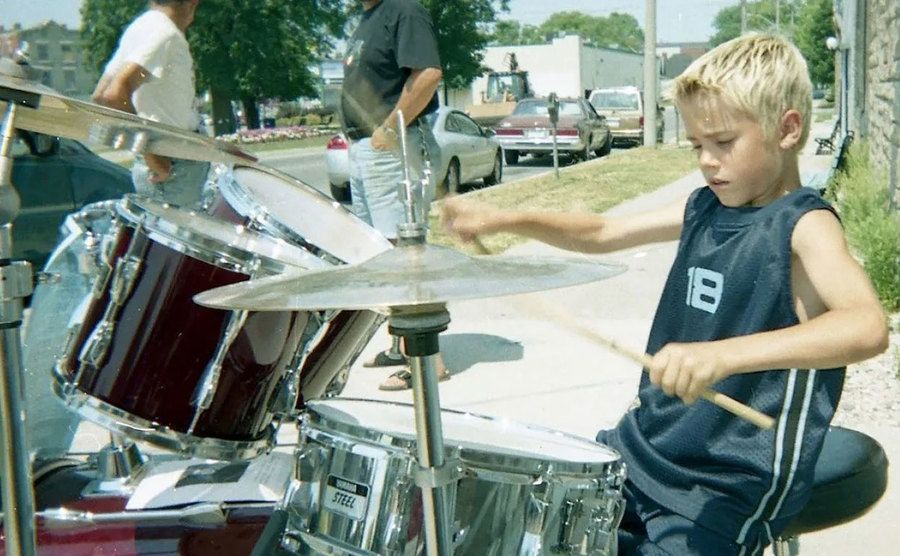 A young Justin Bieber plays the drums on the street.