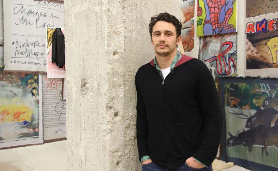 James poses beside his art in a gallery.