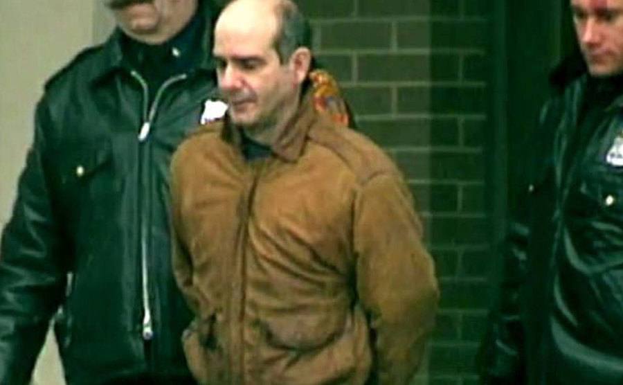 A still of Esposito escorted by police walking in handcuffs.