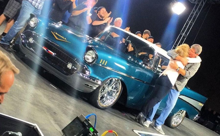 The production team claps as a contestant sees the upgraded car.