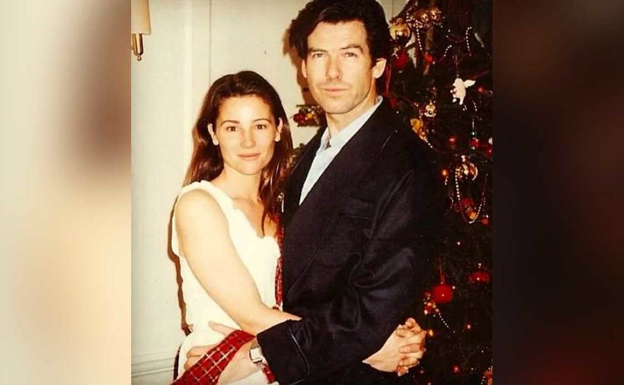 Pierce Brosnan and Keely Shaye Smith embrace beside a Christmas tree.