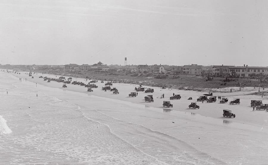 A dated image of cars parked on the beach.