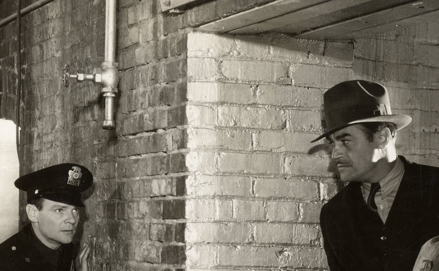 Two police officers lie in wait for a bank robber in a scene from a movie.