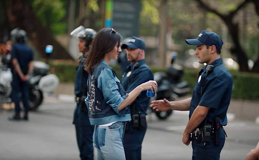 Kendall hands a can of Pepsi to a police officer.