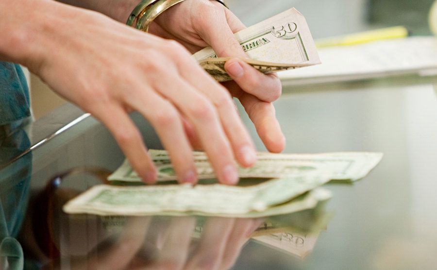 An image of a woman counting dollar bills on a glass counter.