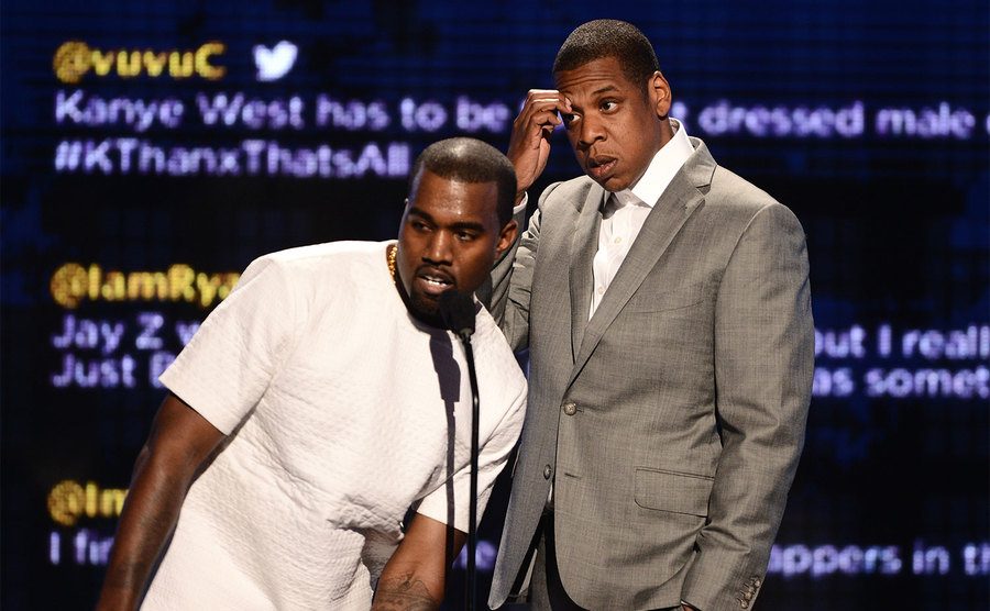 Kanye speaks while Jay Z looks uncomfortable on stage.