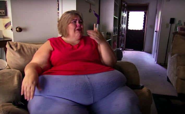 An overweight woman is crying on the couch.