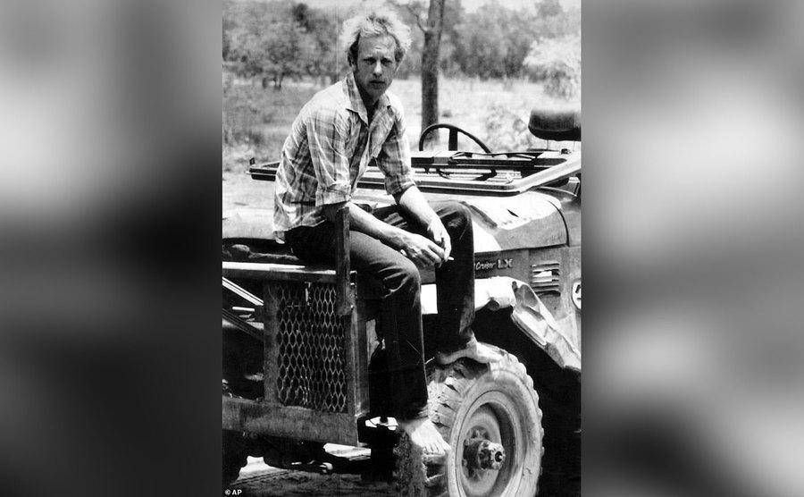 Ansell is sitting on the hood of his tractor.