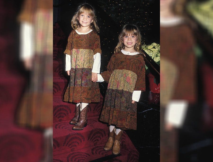 Mary-Kate and Ashley Olsen photographed in 1992 wearing identical brown dresses with cowboy boots.